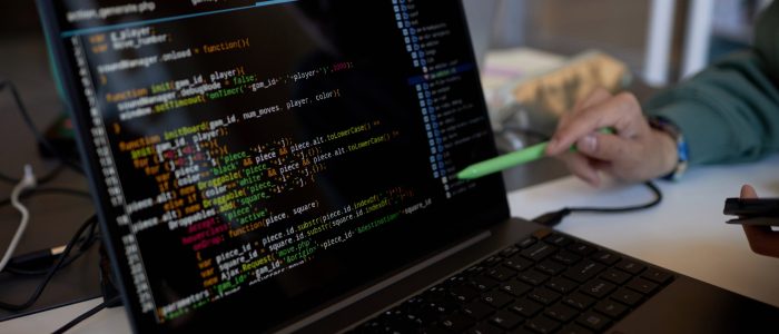 Focus on laptop screen with coded data and pen held by hand of young male teacher or student making presentation of new software